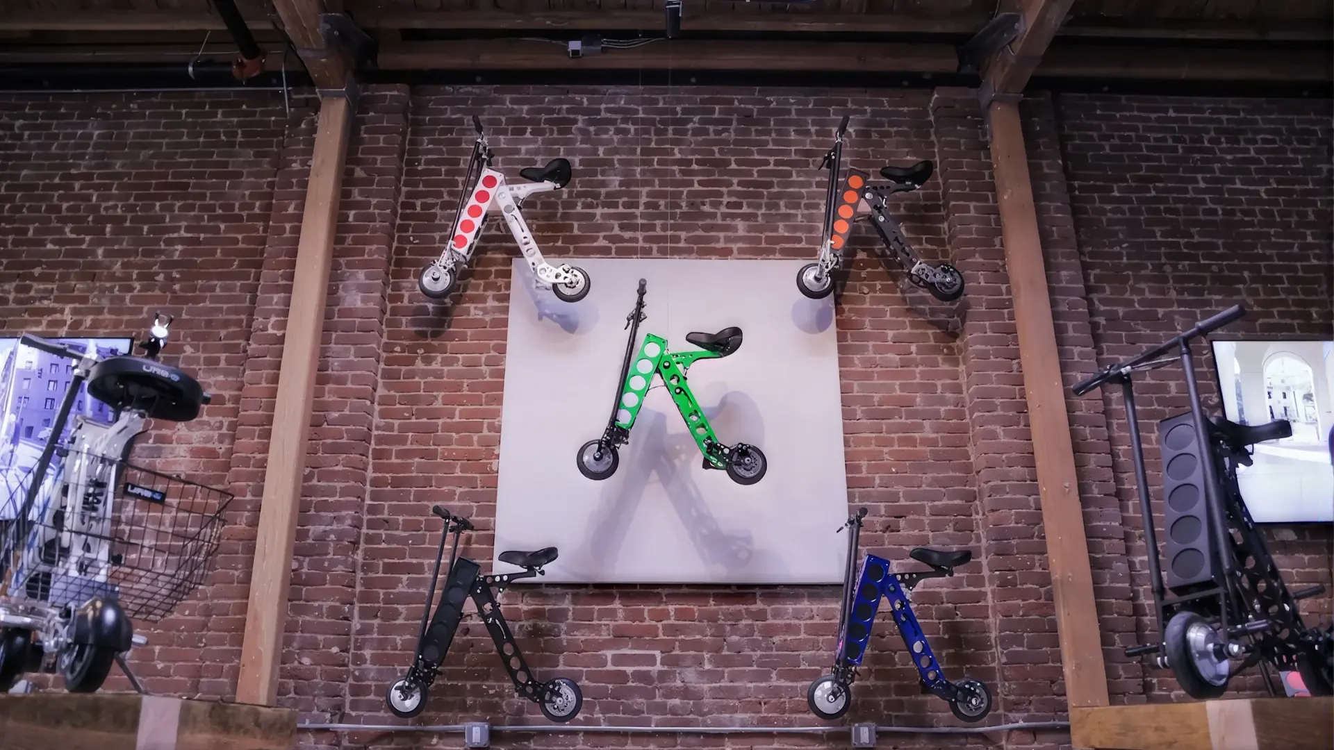 Five URB-E scooters on the brick wall of their Pasadena shop, each in a different frame and insert pairing